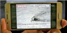  ??  ?? A Pakistani journalist watches a video released by Pakistan’s Navy that allegedly shows an Indian submarine, on a smartphone in Islamabad. — AFP photo