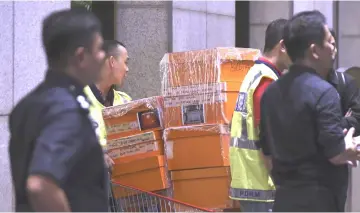  ??  ?? Police personnel push a trolley of boxes believed to contain the luxury branded bags to the main door of a condominiu­m raided. — Bernama photo