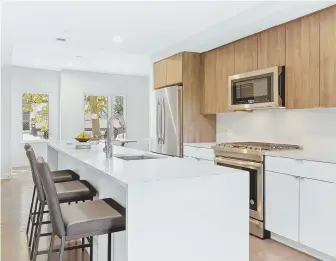  ?? PHOTOS COURTESY RE/MAX DESTINY ?? BRIGHT SPACE: The kitchen has slick European-style white and walnut-finish cabinetry; a long quartz center island with seating, a sink, dishwasher and storage, stainless steel appliances and a glass subway tile backsplash.