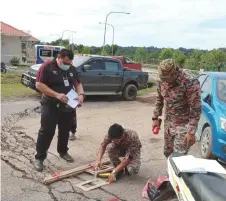  ??  ?? Bomba personnel marks out the gap between the cracks near the clinic seen in the background.