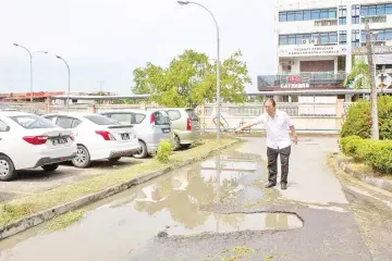  ??  ?? Wong inspecting the puddles on the damaged driveway at the main entrance to Luyang Health Clinic.