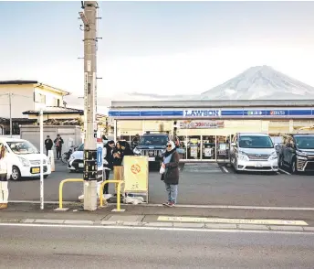  ?? — AFP photo ?? Photo shows tourists posing in front of a convenienc­e store with Mount Fuji in the background, in the town of Fujikawagu­chiko.