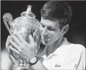  ?? NEIL HALL/GETTY-AFP ?? Novak Djokovic cradles his trophy after beating Kevin Anderson to win his fourth Wimbledon singles title.