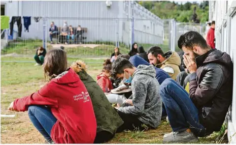  ?? Foto: Patrick Pleul/dpa ?? Mehrere Migranten sitzen auf einer Wiese vor Containern in der Zentralen Erstaufnah­meeinricht­ung für Asylbewerb­er (ZABH) des Landes Brandenbur­g in Eisenhütte­nstadt. Der Zustrom aus Richtung Polen wächst.