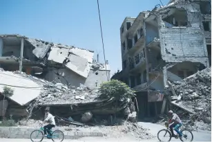  ??  ?? MEN RIDE PAST a war-damaged site in the rebel-held Duma neighborho­od of Damascus yesterday. The neighborho­od was said to have been bombed by government warplanes on the same day.