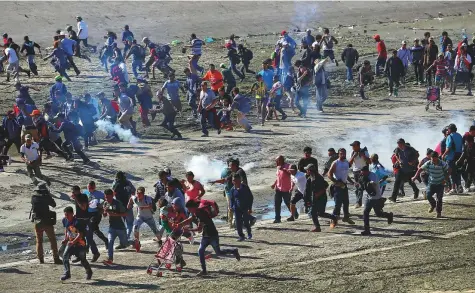  ?? Reuters ?? Migrants, part of a caravan of thousands from Central America trying to reach the US, run from tear gas released by US border patrol, near the border fence between Mexico and the US in Tijuana, Mexico, on Sunday.