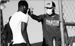  ??  ?? Trainer Joey Pena, right, uses a thermomete­r on the forehead of sophomore running back Gervawn Neville for a temperatur­e check Thursday in Arlington, Texas.