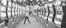  ??  ?? File photo shows an attendant walking between rows of slot machines inside Resorts World Sentosa in Singapore. Growing optimism is seen in Singapore as the overall market condition has improved with higher gaming volume attributab­le to higher patronage...