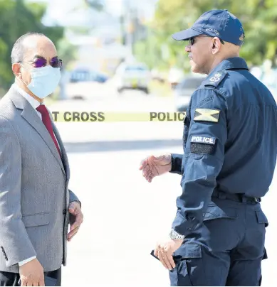  ??  ?? LEFT: Dr Horace Chang (left) minister of national security and Major General Antony Anderson, commission­er of police in dialogue yesterday while at Queens Drive in Horizon Park, Spanish Town, St Catherine, where two lawmen were gunned down and two others injured.