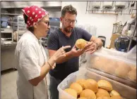  ?? NWA Democrat-Gazette/DAVID GOTTSCHALK ?? Last week, Scott McGehee (right), co-owner and chef of Big Orange and Daymara Baker, founder of the Rockin’ Bakery of Fayettevil­le, examine buns she has baked that will be the type used at the new restaurant at Pinnacle Hills Promenade in Rogers.