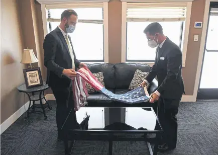  ??  ?? Location leader Al Kamm, left, and funeral director Michael Neel unfold a retired, donated American flag Friday at the All Veterans Funeral & Cremation care center. All Veterans will cut out five stars from the donated flag and attach them to separate certificat­es before the flag is draped over a veteran for cremation.
