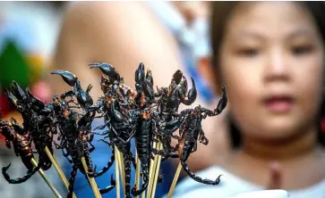  ?? AFP ?? A CHILD looks at scorpions on a stick at a street food market in Chinatown in Bangkok, Thailand.