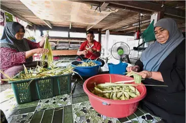  ?? — Bernama ?? Art of weaving an income: Zainab (right), who is helped by her two children Mohd Azwan Ismail and Noraida, preparing the ‘ketupat palas’ in Kampung Bukit Tunggal, Kuala Terengganu.