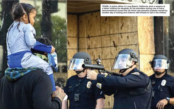  ?? Picture: RICHARD GRANT ?? TENSE: A police officer in Long Beach, California, aims a weapon at a father holding his daughter on his shoulders during one of many demonstrat­ions across the US which saw peaceful protests marred by another day of looting and violence with threats to call in the military