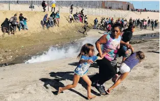  ?? PHOTO: REUTERS ?? No welcome mat . . . A migrant woman from Honduras, part of a caravan of thousands of people from Central America trying to reach the United States, runs away from tear gas with her twin daughters, in front of the border wall between the US and Mexico, in Tijuana on Monday.