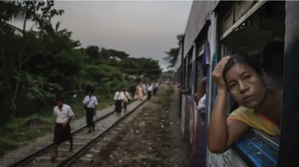  ??  ?? A passenger looks out of a Circle Line train as others who just disembarke­d walk along the tracks. The 45-kilometre line loops around Burma’s largest city.