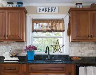  ??  ?? Right: A garland of dried orange slices accents the simple kitchen valance and sets off a wooden star propped on the sill. A bucket of blooms and a handmade Bakery sign further enhance the window.