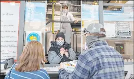  ??  ?? Cashier Demy Somera, center, and chef and owner Floriana Pastore watch as people receive their order in the parking lot of the Pinball Hall of Fame on Saturday.