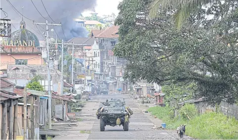  ?? AFP ?? A Marines armoured personnel carrier speeds away as black smoke billows from burning houses after military helicopter­s fired rockets at militant positions in Marawi yesterday.