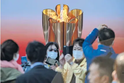  ??  ?? FLAME OF HOPE: People wearing face masks take pictures in front of the Tokyo 2020 Olympic flame, which is displayed outside Sendai railway station, Miyagi prefecture.