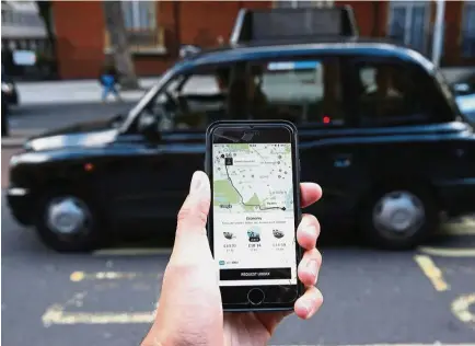  ?? — AFP ?? London taxi affair: A woman holding a smartphone showing the app for Uber in London. Uber is reported to be prepared to make concession­s to restore its revoked London taxi licence.