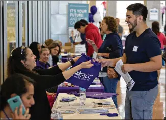  ?? DAULTON VENGLAR / AMERICAN-STATESMAN ?? Angelica Diaz-Miranda De La Rosa hands out a bag at a career fair at the ACC Highland campus on Friday. The conversion of the run-down Highland Mall into an innovative college campus played a part in the school’s CEO getting a seat on the League for...