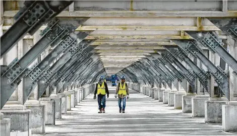  ??  ?? Melissa Phillip / Staff photograph­er Workers make their way beneath the main pipe rack at Cameron LNG in Hackberry, La. More than 8,000 people are working day and night to bring the liquefied natural gas plant’s first production unit into operation over the next few months.