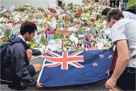  ?? ANTHONY WALLACE/AFP/GETTY IMAGES ?? Students display the New Zealand national flag next to flowers during a vigil in Christchur­ch on March 18, three days after a shooting incident at two mosques that killed 50 people.