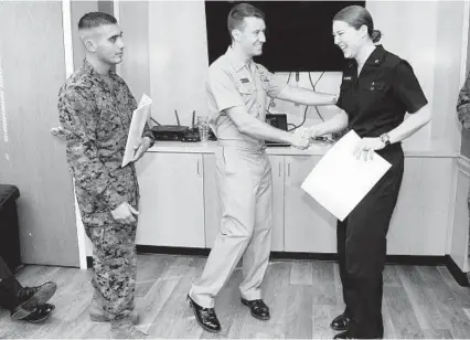  ?? PAUL W. GILLESPIE/BALTIMORE SUN MEDIA GROUP ?? Navy Lt. Sean Heenan, center, company officer for the Naval Academy’s 12th Company, shakes hands with senior McKenna Niemer Thursday as she gets her service assignment as a Marine Corps aviator, her first choice. At left is Marine Staff Sgt. Jesse...