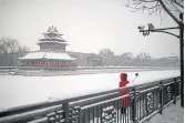  ??  ?? A woman wearing a face mask takes a selfie after a snowfall outside the Forbidden City in Beijing.