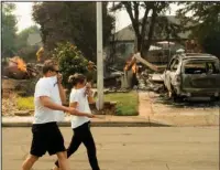  ?? The Associated Press ?? GROWING RAPIDLY: A couple, who declined to give their names, passes homes leveled by the Carr Fire in Redding, Calif., on Friday. Officials say the extremely erratic wildfire in and around the city of Redding is growing rapidly amid scorching temperatur­es, low humidity and windy conditions.