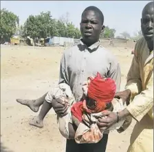  ??  ?? A man carries an injured child following a military air strike Tuesday at a camp for displaced people in Rann, Nigeria.
