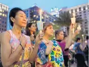  ?? RICARDO RAMIREZ BUXEDA/ORLANDO SENTINEL ?? Sam Jitaree, left, and Devi Thompson, of Orlando, hold candles as bells ring for each of the victims of the Pulse nightclub shooting during a vigil at the Dr. Phillips Center for the Performing Arts.