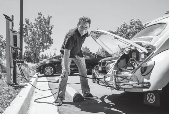  ?? IRFAN KHAN/LOS ANGELES TIMES ?? Mark Wagner, who converted his 1962 VW Beetle ragtop from gas to electric, charges it April 19 at a charging station in Irvine, California.