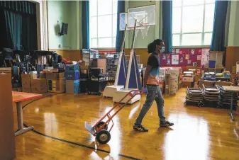  ?? Photos by Gabrielle Lurie / The Chronicle ?? Head custodian Ashanti Lewis organizes the assembly room at Sankofa United Elementary on the first day of school — with students at home participat­ing in classes via computer screens.