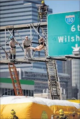  ?? Marcus Yam Los Angeles Times ?? FIREFIGHTE­RS and California Highway Patrol officers watch as Alexander Dunn backflips onto a massive inflatable cushion Wednesday on the 101 Freeway.