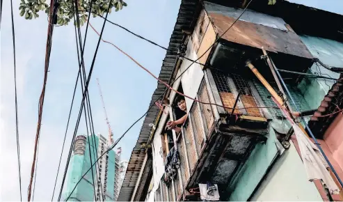  ?? VEEJAY VILLAFRANC­A Bloomberg ?? A RESIDENT looks out from a low-cost house as a residentia­l developmen­t stands under constructi­on in the background in Mandaluyon­g, Metro Manila, Philippine­s. Children are generally more likely to earn incomes similar to their parents in nations with higher income inequality. |