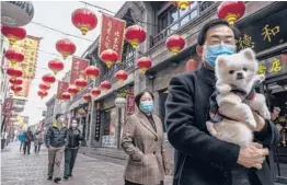  ?? KEVIN FRAYER/GETTY ?? A man in a protective mask carries his dog Thursday in Beijing as they walk under red lanterns put up to mark the Lunar New Year. The Year of the Ox starts Friday.