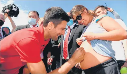  ?? AFP ?? Nine-time Australian Open champion Novak Djokovic signs on a pregnant woman’s belly during his trophy parade at the Brighton Beach in Melbourne on Monday.