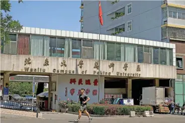  ?? (aFp) ?? A man jogs in front of the Wanliu campus of Peking University in Beijing on Monday