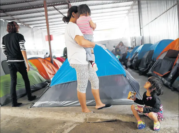  ?? MARIO TAMA/GETTY ?? A Honduran mother stands with her daughters in the migrant shelter where they are currently living near the U.S.-Mexico border on April 4in Tijuana, Mexico. The woman said they are on the waiting list to apply for asylum in the U.S. and must wait at the shelter.