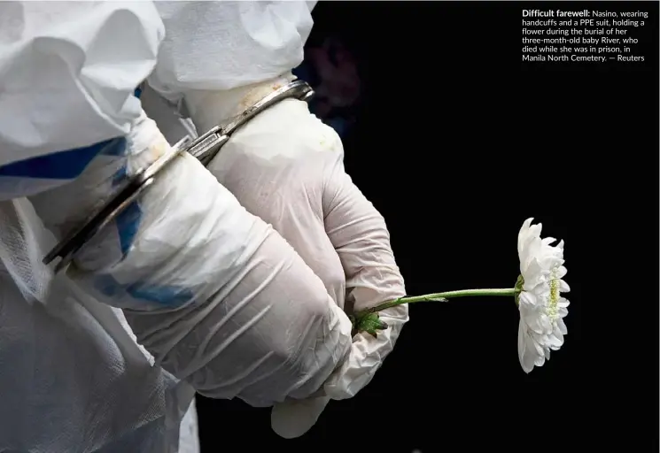  ?? — Reuters ?? Difficult farewell: Nasino, wearing handcuffs and a PPE suit, holding a flower during the burial of her three-month-old baby River, who died while she was in prison, in Manila North Cemetery.