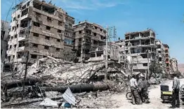  ?? HASSAN AMMAR/AP 2018 ?? People stand in front of damaged buildings in the town of Douma last April. Douma, which is near Damascus, was the site of a suspected chemical weapons attack.