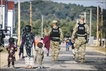  ?? Barbara Davidson Associated Press ?? MILITARY POLICE walk past Afghans at the Village at Ft. McCoy, Wis., in September. The fort is one of eight military installati­ons across the country that are temporaril­y housing tens of thousands of Afghans.