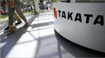  ?? THE ASSOCIATED PRESS ?? Visitors walk by a Takata Corp. desk at an automaker’s showroom in Tokyo. Japanese auto parts maker Takata Corp. pleaded guilty to fraud Monday and agreed to pay $1 billion in penalties for concealing an air bag defect blamed for at least 16 deaths,...