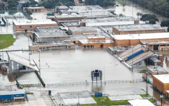  ?? Brett Coomer / Houston Chronicle ?? Above: A football field at C.E. King High School is flooded by rising waters on Tuesday. The high school football season was supposed to start this weekend, but will be delayed for Houston area programs. At right: People line up to volunteer Wednesday...