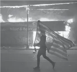  ?? JULIO CORTEZ/AP ?? A protester carries a U.S. flag upside down next to a burning building on May 28 in Minneapoli­s during protests over the death of George Floyd.