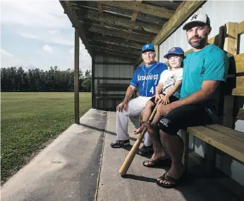  ??  ?? Baseball runs in the blood of families in Marysburg and has for a century now. From left in the dugout are coach Wayne Strueby, his four-year-old grandson Hudson and son Curtis. The passion for baseball in Marysburg has “carried down the generation­s,” Strueby says.