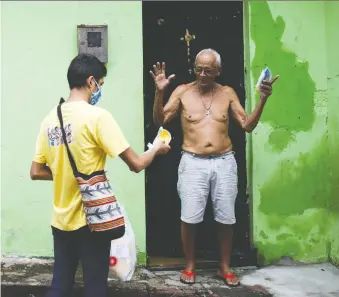  ?? REUTERS ?? Catholic Church seminarian Renan Alberto Lima de Oliveira delivers a protective mask to a resident in the Educandos slum in Manaus, Brazil, where deaths are mounting in the COVID-19 crisis.