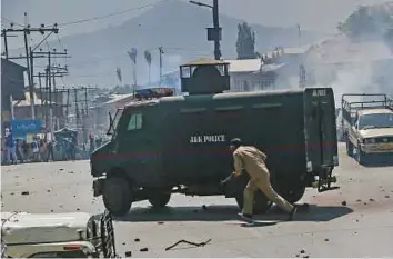  ?? AP ?? A policeman takes cover behind an armoured vehicle from stones thrown by protester after ■ police stopped the funeral procession of a man who died after a paramilita­ry vehicle hit him.